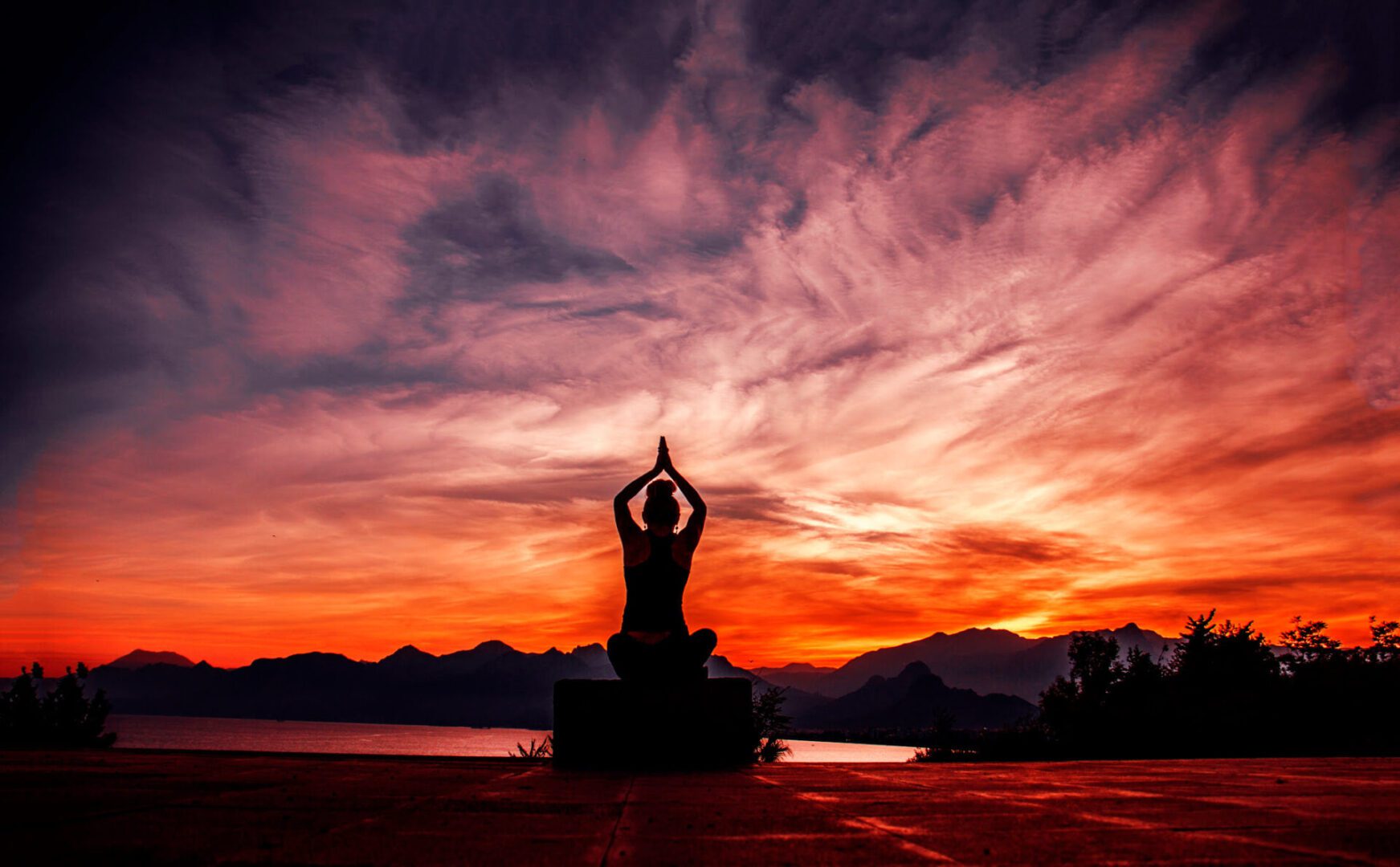 Person meditating at sunset by mountains.