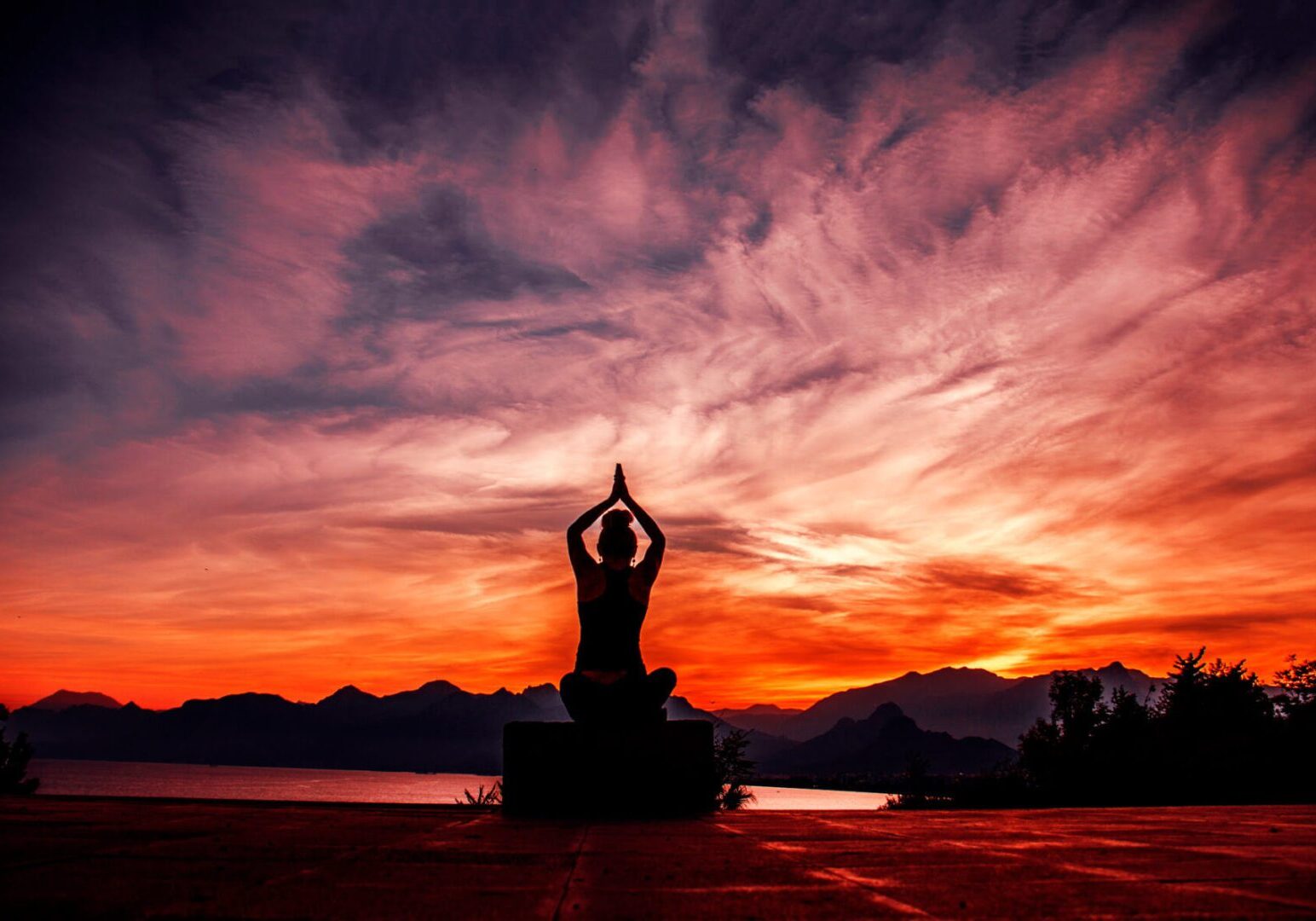 Person meditating at sunset by mountains.